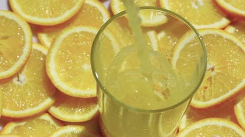 Orange Juice Pouring into Glass With Orange Slices
