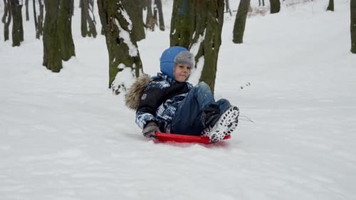 Happy smiling boy riding down the snowy hill on plastic sleds