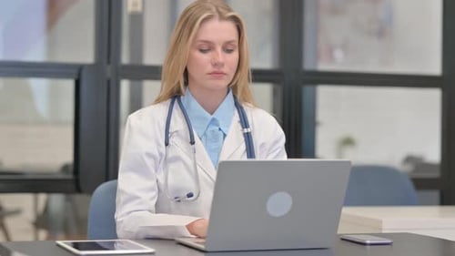 Junge Ärztin schaut in die Kamera, während sie im Krankenhaus am Laptop arbeitet