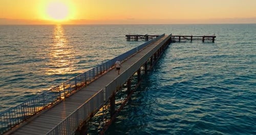 Aerial View of a Man Running Along a Pier on the Seashore at Sunset