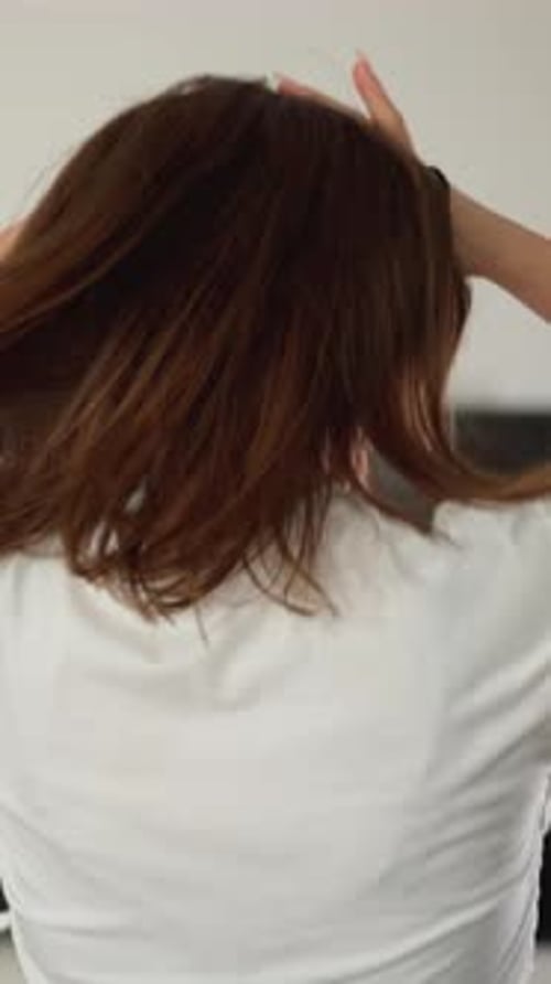 Woman Styling Auburn Hair in Ponytail Indoors