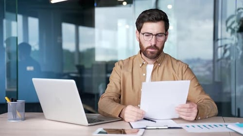 Concerned Man Reviews Documents at Office Desk