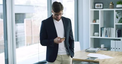 4k video footage of a handsome young businessman using a cellphone while standing in his office