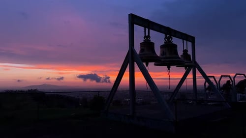Drei Glocken in der Morgen- oder Abenddämmerung mit der Landschaft im Hintergrund, wunderschöner bunter Himmel, Glockenturm