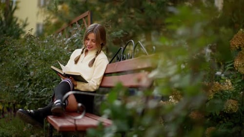 Beautiful Girl with Pigtails Sitting on a Bench and Reading a Book Reading in the Park