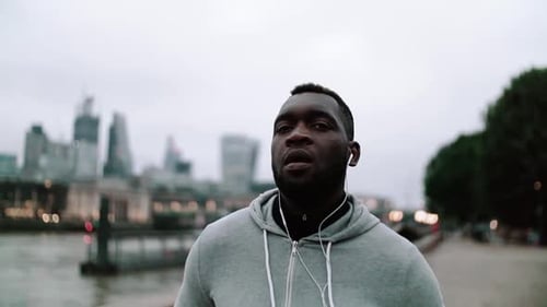 Sporty Black Man Runner With Earphones Running On The Bridge In A City.