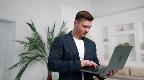 Geschäftsmann tippt auf dem Laptop, schließt das Gerät und schaut in die Kamera.