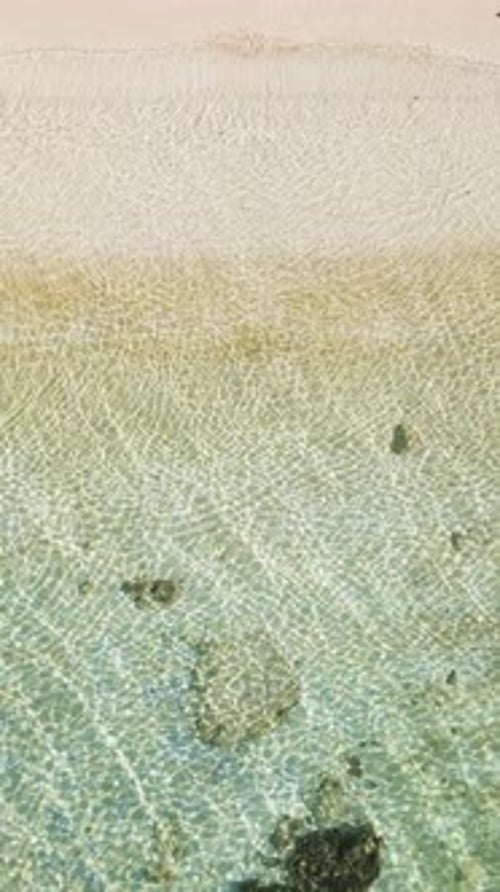 Top view of a white sandy beach with clear water.
