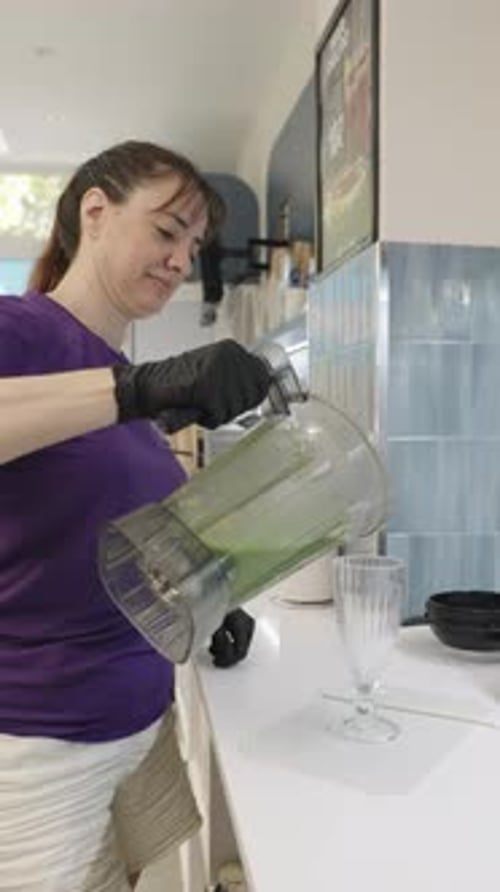 Woman Pouring Green Smoothie Into Glass in Kitchen