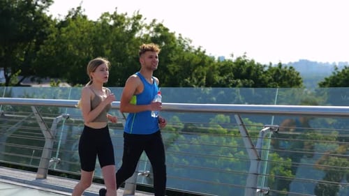 Happy Couple Running Across the Bridge Taking a Break Man Holding Bottle of Water Exercising Jogging