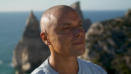 Handsome man smiling relaxing on cliff overlooking tranquil ocean view summer vacation
