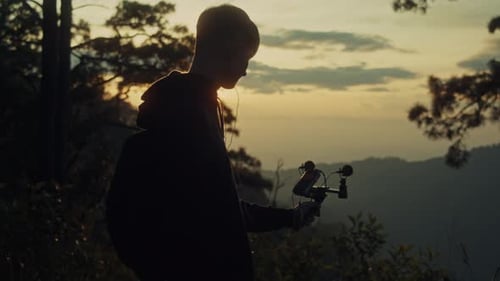 Ein junger Mann hält ein Mikrofon in der Hand, um seine Umgebung vor dem Hintergrund eines Sonnenuntergangs in den Bergen aufzunehmen