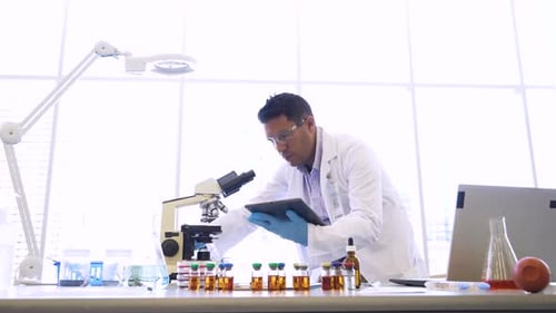 Hispanic scientist uses digital tablet at microscope in science laboratory