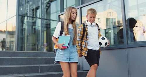 School couple. Friendly children with backpacks walking on stairs near school after lessons. Talking