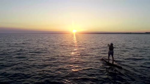 Person Paddleboarding on Calm Sea at Sunset