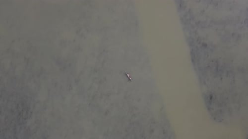 Overhead top down aerial view of tiny fishing boat in middle of brown river
