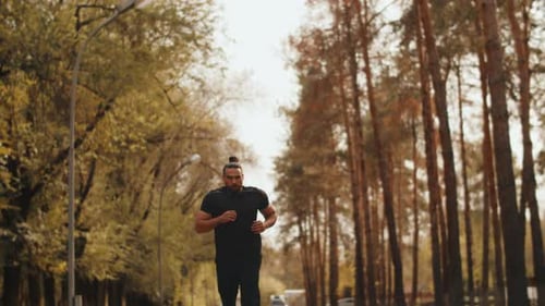 Young Muscular Athlete in Black Sportswear Running Unhurriedly on an Alley in an Autumn City Park on