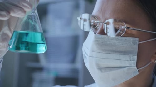 Une chercheuse clinique examine un liquide dans une fiole Erlenmeyer en laboratoire