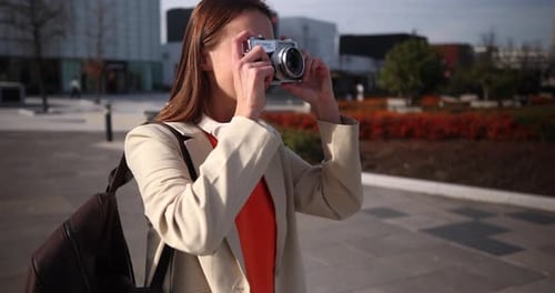 Attractive woman with headphones taking pictures with a vintage camera in a modern city square, then
