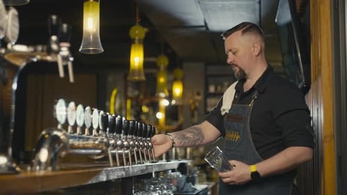 A Bartender Pours Beer From the Tap Into a Glass on the Bar