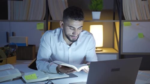 Focused Man Reads Book at Desk Late Night