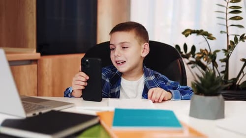 Boy Using Phone at Desk for Online Learning