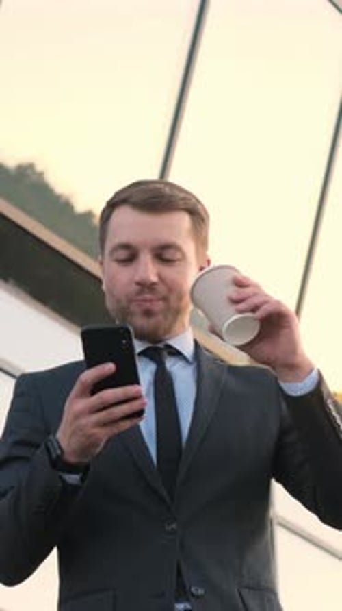 Man in Suit Using Phone and Drinking Coffee