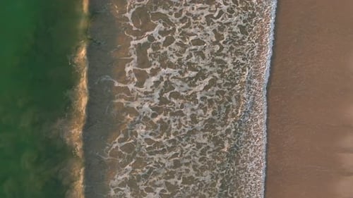 Gentle waves washing onto a sandy beach with clear green water meeting the tan shoreline in a beauti