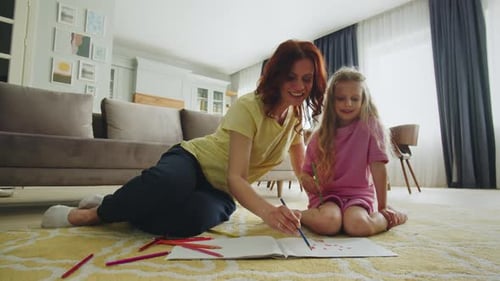 Smiling Mother and Daughter Sit in the Hall on the Floor and Draw Together Preparation for Art