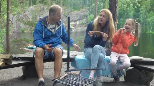 A Couple with a Child Grilling in the Forest on the Shore of the Lake
