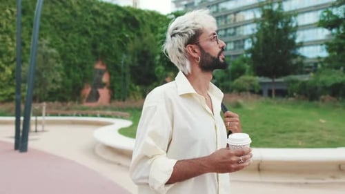 Young Man Walking Through City Park with Coffee