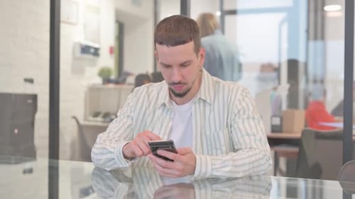 Creative Young Man Browsing Internet on Phone in Office