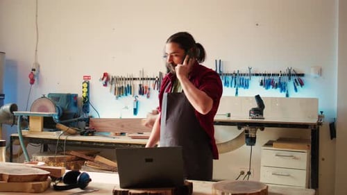 Un menuisier dans un atelier d'assemblage discute sur smartphone avec un client