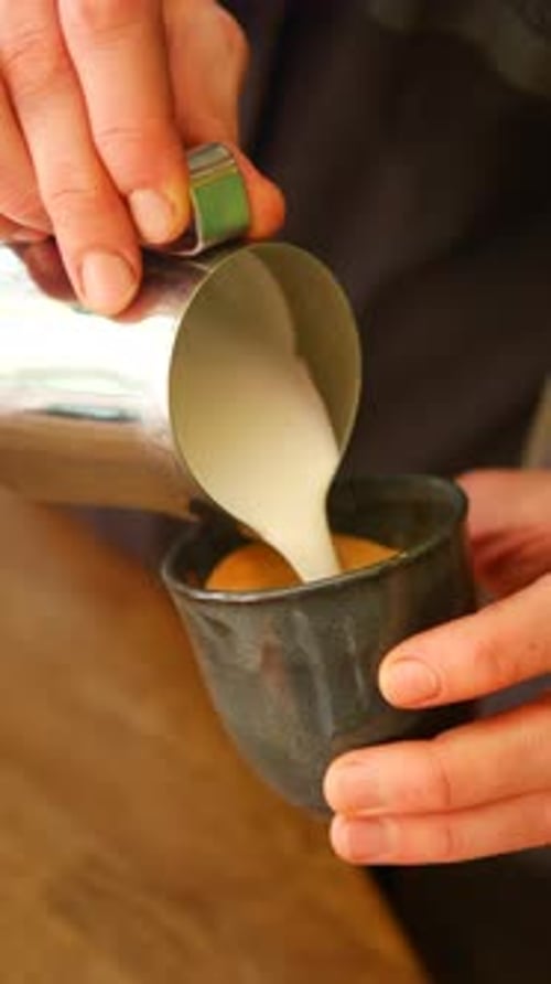 Pouring Steamed Milk Into a Dark Coffee Cup in a Cafe
