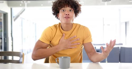 Parlant passionnément, un homme en chemise jaune faisant des gestes avec les mains à la table de la maison