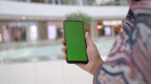 Halten Sie ein Smartphone mit einem grünen Bildschirm in einem Einkaufszentrum