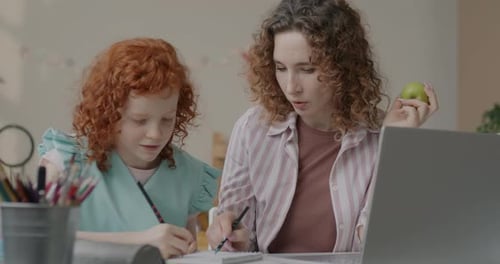 Woman Helps Child with Homework at Table