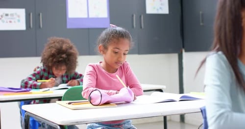 In school, girl writing in notebook at classroom desk, concentrating on work