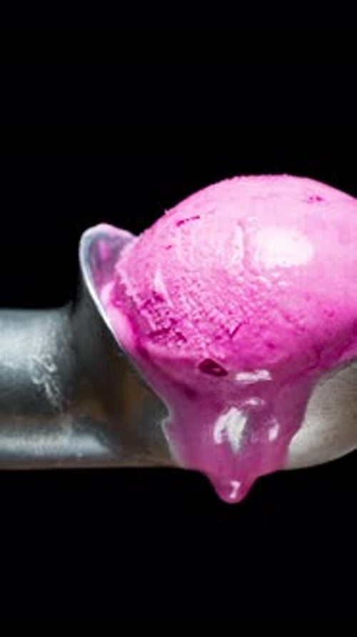 Vertical video. The ice-covered ice cream scoop and the pink ice cream ball melt, drip down