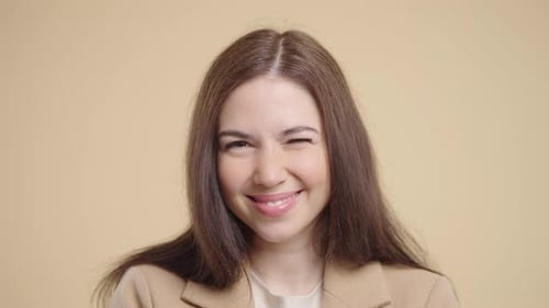 Smiling Young Woman Winks, Studio Shot on Beige
