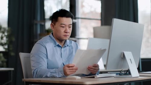 Focused Asian Middle Aged Man Checking Financial Reports Reading Documents and Comparing Them with