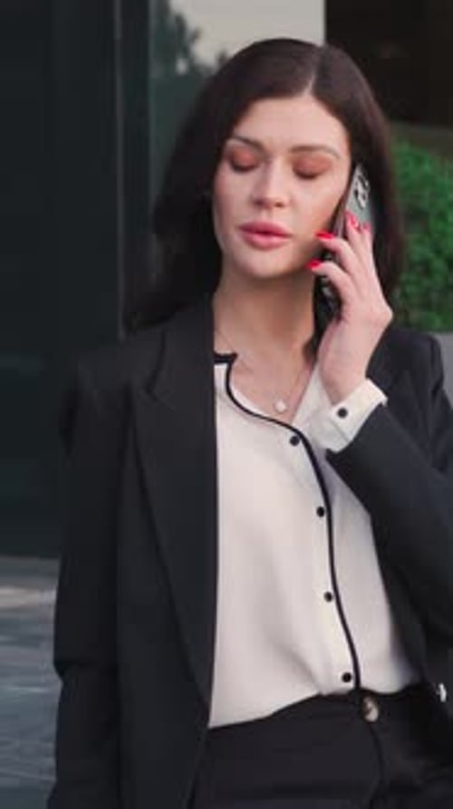 Attractive brunette businesswoman is sitting on the stairs in front of a glass business center.