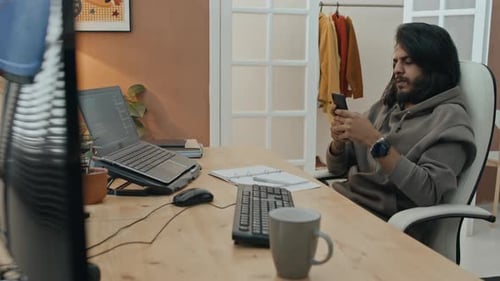Männlicher Programmierer tippt auf dem Smartphone, während er von zu Hause aus arbeitet