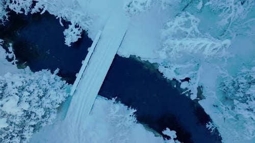 Snow-covered Bridge Over The Stream By The Forest In Winter. - aerial ascend shot