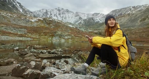 Hiker Using Smartphone Sitting Near Mountain Lake Enjoying Landscape
