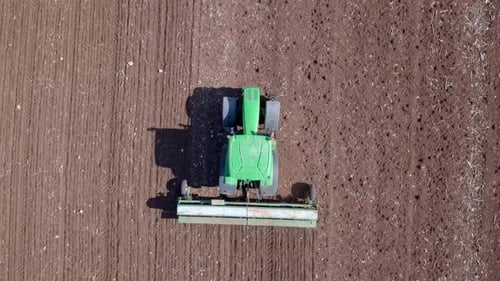 Green Tractor cultivating and seeding a dry field - Top down aerial footage