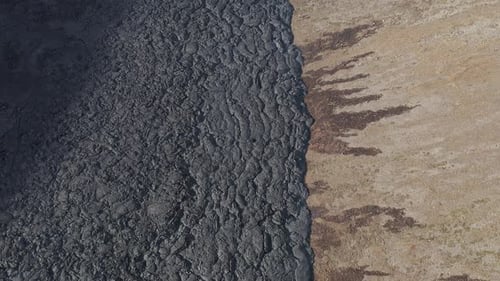 Black solid lava field on slope of valley mountain in Iceland, aerial