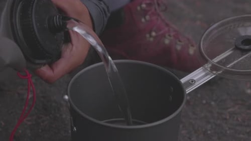 Two women on a backpacking trip pour water into a camp stove to cook a dehydrated meal in the Olympi