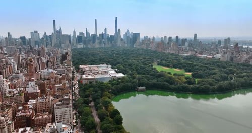 Lovely green area of Central Park in New York neighboring with dense city architecture.