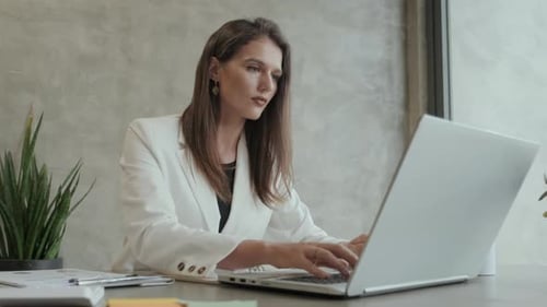 Woman Typing on Laptop and Writing at Desk